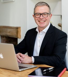 Photo of Tim Davies sitting at his desk in business suit with laptop open. My mentoring services.