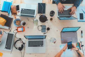 Photo of five laptops, coffee cups, and mobile phones on a desk.