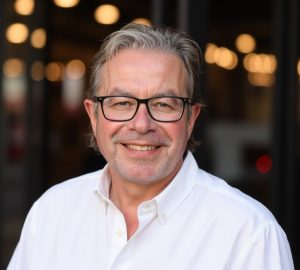 Tim Davies wearing a white business shirt, standing outside with blurred lights in the background.