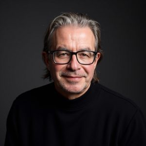 Tim Davies dressed in a dark sweater against a dark background.