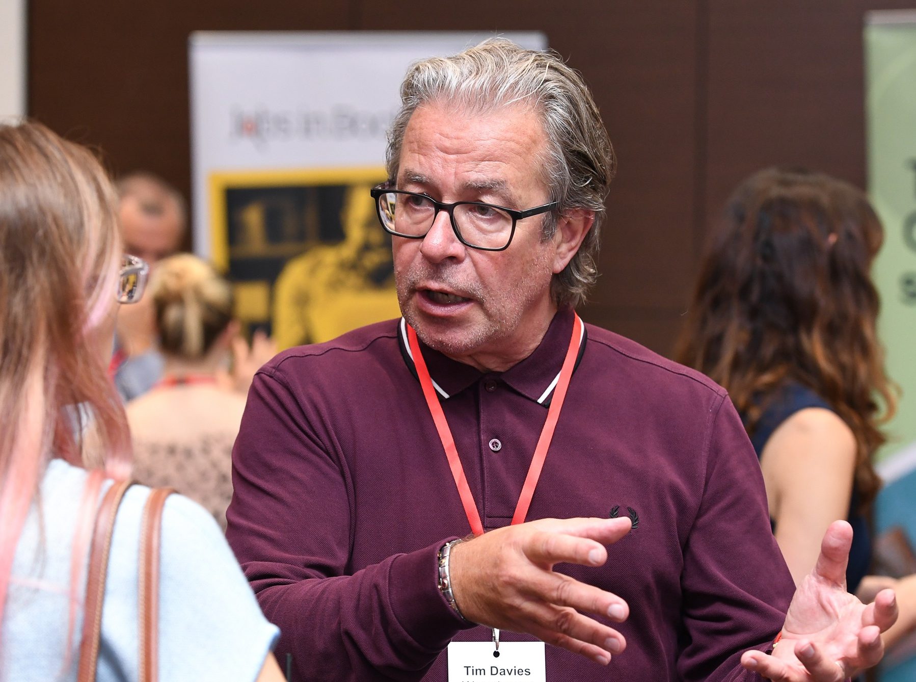 Tim Davies at a trade event, dressed in a casual shirt, in conversation with a woman.