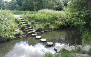 Photo of a stream with stone steps leading down one bank, stepping stones across it, and stone steps leading up the opposite bank.