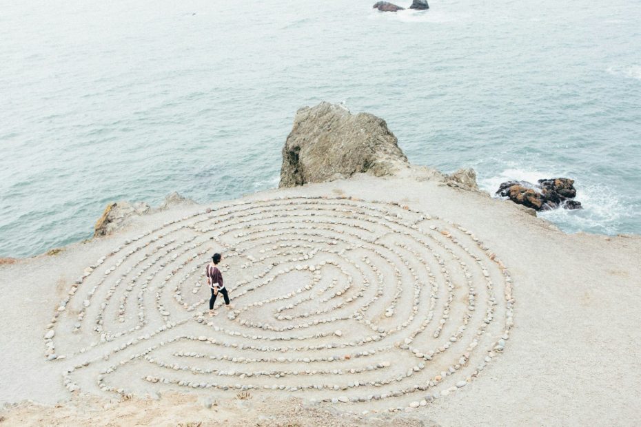 Photo taken from above of a man walking into a circular, ankle-high maze, around 20 metres across, created on a sandy beach.