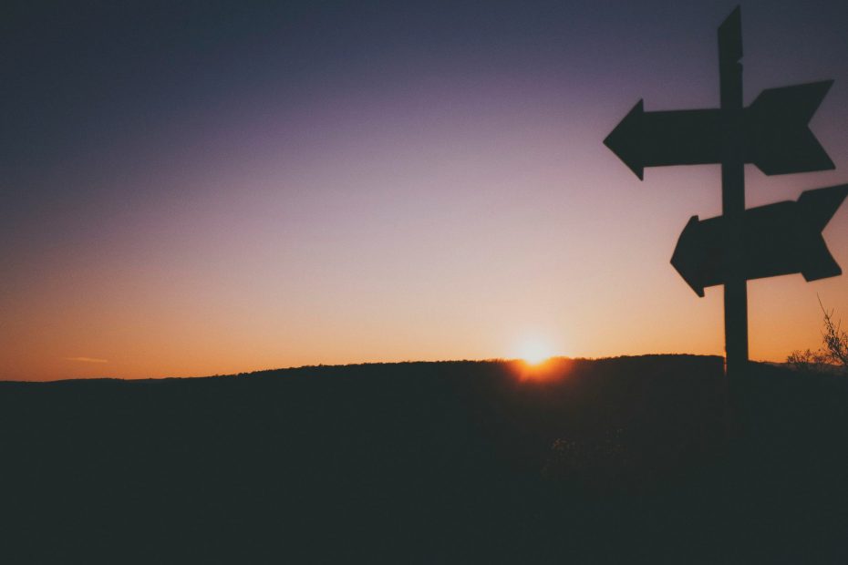 Sunset over land with part of a signpost in silhouette on the far right hand side.