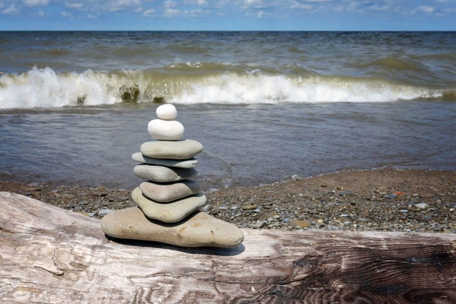 Stack of 7 or 8 large pebbles placed on rocks next to a crashing wave.